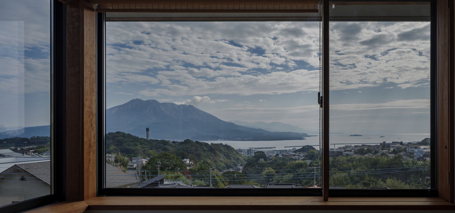 室内から窓越しに望む、雄大な桜島と穏やかな海、緑豊かな街並みが広がる絶景の様子。