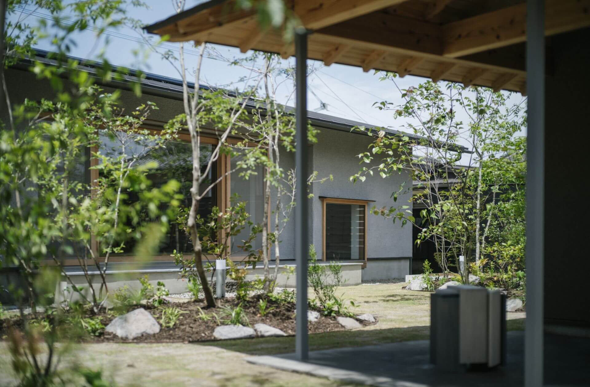 緑の芝生の庭で過ごす夫婦と二匹の小型犬、モダンな家を背景にした穏やかな屋外の様子。
