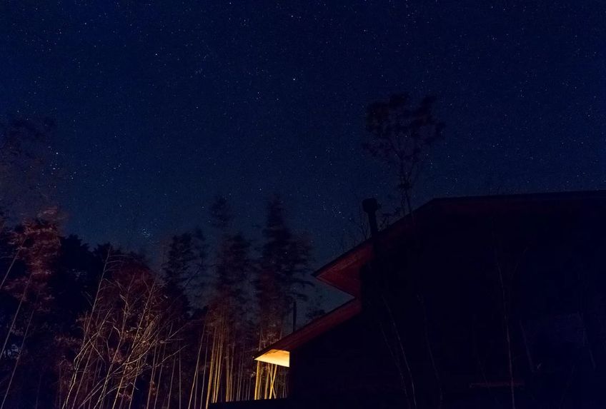 闇夜に森に囲まれたモダンな家と、無数の星が見える、静かな夜景の様子。