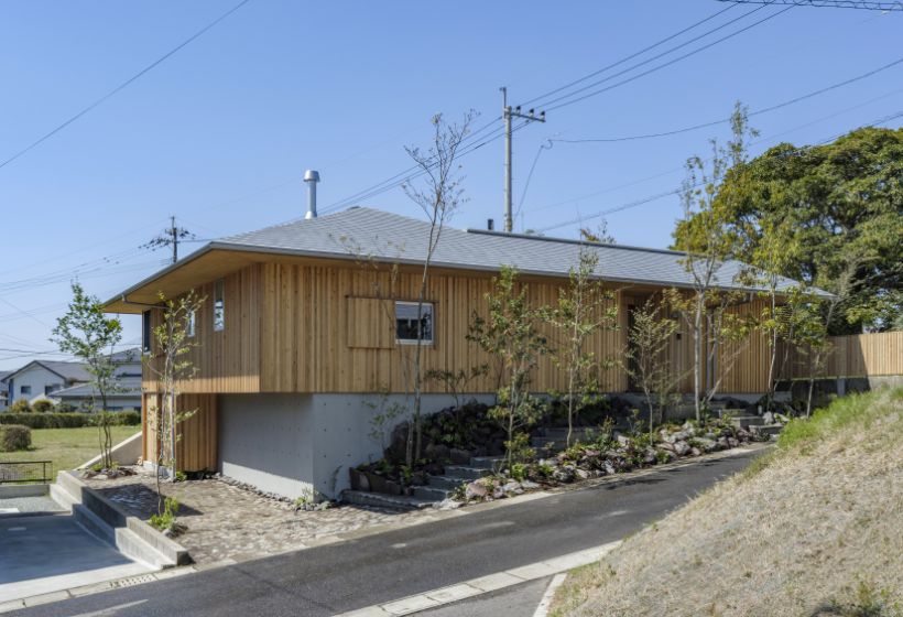傾斜地に建つ木製外壁の平屋。オーバーハングで空中に張り出した独創的な外観の様子